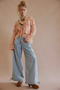 Dettaglio dei jeans a gamba larga azzurri con lacci alle caviglie e pieghe in vita
