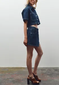 Dettaglio di un completo in denim blu scuro con cuciture bianche e bottoni argento
