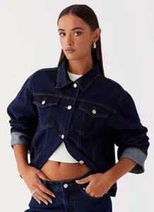 Detail of dark blue denim jacket with silver metal buttons and chest pockets on model