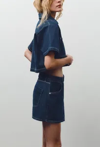 Dettaglio del set in denim blu scuro con camicia e minigonna e cuciture bianche a contrasto