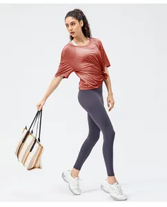 Detail van losse baksteenrode sporttop en grijspaarse yoga-leggings met hoge tailleband