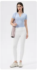 Women's light blue yoga top with front zipper and white leggings set in studio