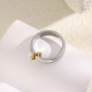 Minimalist silver stainless steel ring featuring a gold circular buckle charm on a pedestal