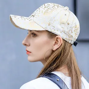 Detail of white cotton baseball cap with gold bird and floral prints and black back strap
