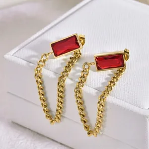 Détail de boucles d'oreilles géométriques en or avec zircon rouge et fines chaînettes