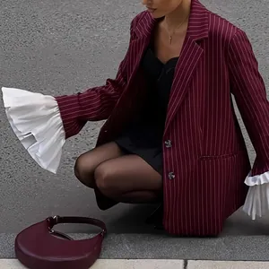 Detail of burgundy striped blazer featuring oversized white pleated ruffles on the cuffs