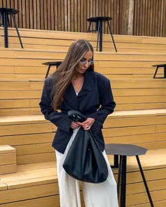 Detail of a black leather handbag with knotted handle paired with a navy pinstripe blazer