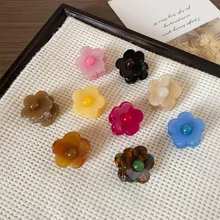 Top view of mini floral resin hair claws in nine colors on a white textured mat