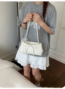 Détail d'un sac à bandoulière blanc crème avec nœud 3D et bandoulière à pois noirs