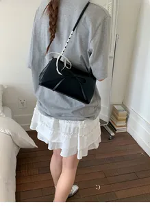 Détail du sac à bandoulière en similicuir noir avec nœud et ruban à carreaux