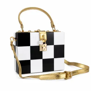 Detail of checkered acrylic box bag with golden metal handle and flower charm