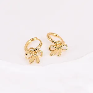 Detail view of elegant golden bow dangle earrings on a minimalist white background