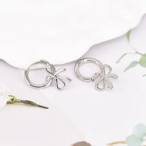 Close-up of silver bow pendant earrings on a white textured plate with greenery