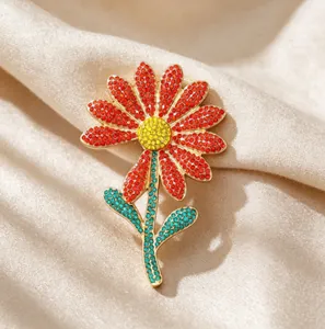 Detail of red daisy brooch with sparkling crystals on gold metal base and green leaves
