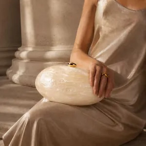 Détail d'une pochette en acrylique marbré blanc avec fermoir doré et robe en soie champagne