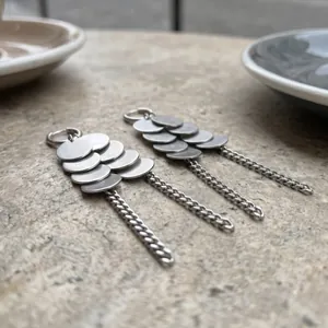 Détail des boucles d'oreilles à disques argentés et pompons au style géométrique pur