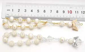 Detail view of rosary bracelets with rose beads and angel wings charms next to a ruler