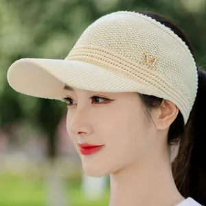 Detail of beige knitted visor hat with gold metal M logo on side for sun protection