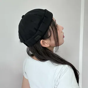 Side-rear view of a minimalist black knit Miki hat featuring a small side woven label