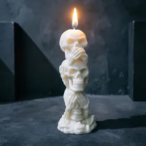 Detail of three stacked skulls soy wax candle with bright flame on dark background