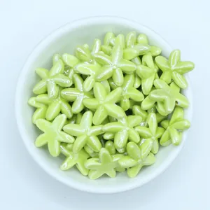 Macro detail of glossy light green starfish ceramic beads in a white bowl for DIY jewelry