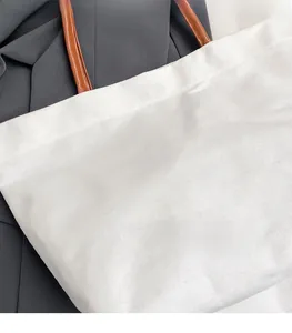 Close-up of white canvas tote bag with brown leather handles and minimalist stitching