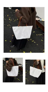 Detail of a large white canvas tote bag with brown straps styled on a woman's shoulder
