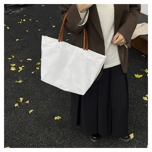 Side view of a white canvas tote bag with brown leather handles in an autumn street setting
