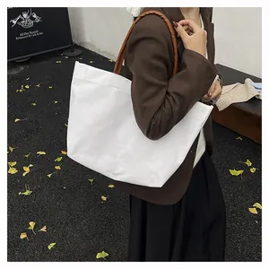 Outdoor shot of a minimalist white canvas tote bag with brown handles on a model's shoulder