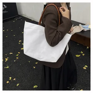 Close-up of minimalist white canvas tote bag with brown leather straps worn by model