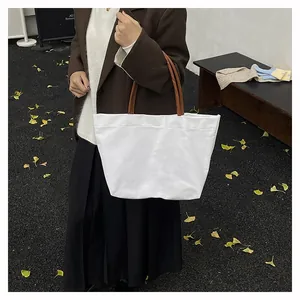 Outdoor shot of a minimalist white canvas tote bag with brown leather handles