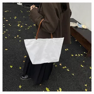 White canvas tote bag with brown leather handles displayed on autumn ginkgo leaves