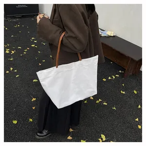 Lifestyle shot of a white large canvas tote bag with brown handles in an autumn street setting