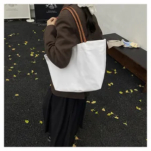 Minimalist white canvas tote bag with brown straps styled on autumn pavement
