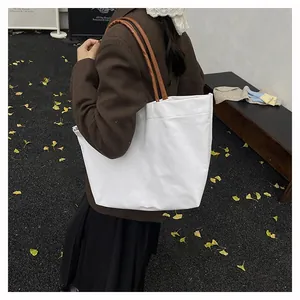 Detail of white canvas tote bag with brown leather handles worn by a model in autumn