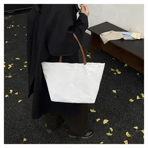 Minimalist white canvas tote bag with brown leather handles worn by a model in a dark coat