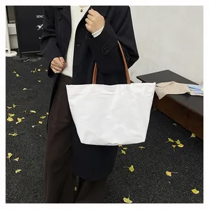 White canvas tote bag with brown leather straps shown in a stylish outdoor autumn setting