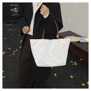 Minimalist white canvas tote bag with brown straps styled with a long black winter coat