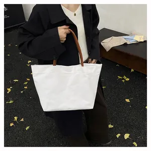 Close-up of white canvas tote bag with brown leather handles worn by a model outdoors