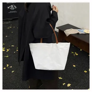 Detail of a large white canvas tote bag with brown leather handles in a street setting