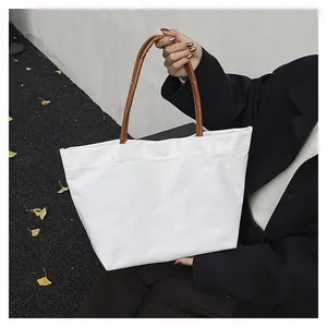 Detailed shot of white canvas tote bag with brown handles carried by a model in a black suit