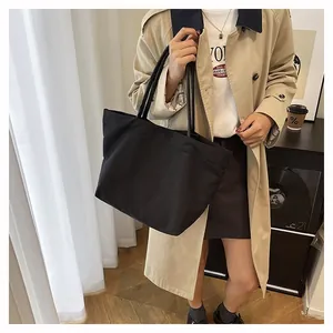 Close-up of a minimalist large capacity black canvas tote bag worn by a model in daily use