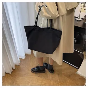 Minimalist large black canvas tote bag with slim handles shown in a lifestyle setting