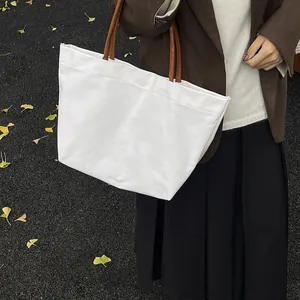 Large white canvas tote bag with brown straps shown in an autumn street setting