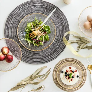 Hammered glass bowl set with gold rims and woven placemats on a white tabletop