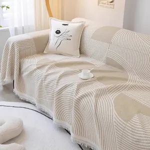 Détail du tissage gaufre et motif géométrique sur jeté de canapé beige à pompons courts