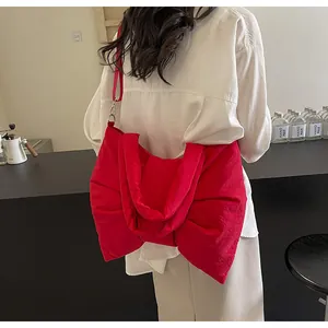Model view of large red bow-shaped tote bag worn as a shoulder bag in a cafe setting