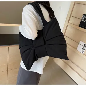 Detail of a black oversized bow tote bag made from soft quilted fabric shown on a shoulder