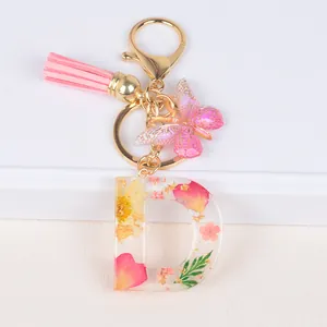Detail of resin letter D keychain with dried flowers, pink tassel and butterfly charm