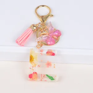 Close-up of resin letter E keychain with dried flowers, pink tassel and butterfly charm